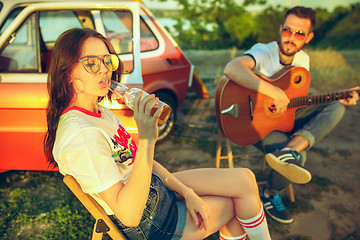 Image showing Couple sitting and resting on the beach playing guitar on a summer day near river