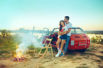 Image showing Couple sitting and resting on the beach playing guitar on a summer day near river