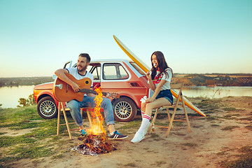 Image showing Couple sitting and resting on the beach playing guitar on a summer day near river