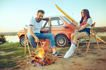 Image showing Couple sitting and resting on the beach playing guitar on a summer day near river