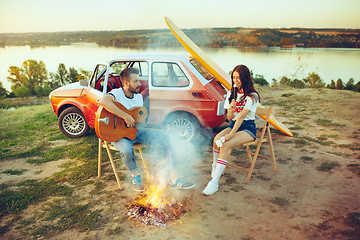 Image showing Couple sitting and resting on the beach playing guitar on a summer day near river