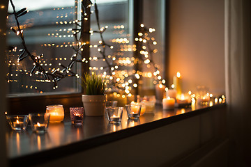 Image showing candles burning on window sill with garland lights