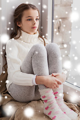 Image showing sad girl sitting on sill at home window in winter