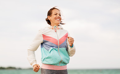 Image showing smiling woman running along beach