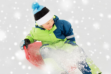 Image showing happy boy sliding on sled down snow hill in winter