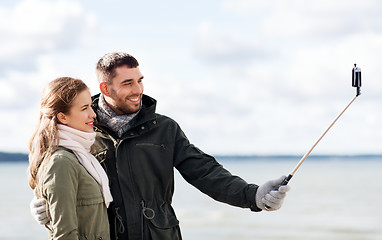 Image showing happy couple taking selfie on beach in autumn