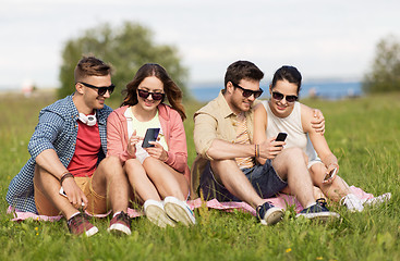 Image showing smiling friends with smartphones sitting on grass