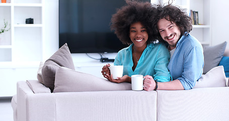 Image showing multiethnic couple sitting on sofa at home drinking coffe