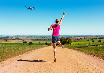 Image showing Woman leaping for joy along dirt road flying a drone