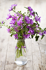 Image showing Wild violet flowers in glass bottle on rustic wooden table.