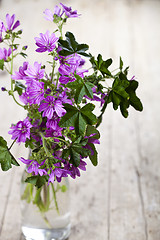 Image showing Wild violet flowers in glass bottle on rustic wooden table.