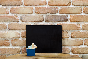 Image showing Blank clean blackboard an chalk on wooden table at brick wall. 