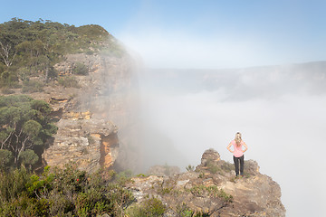 Image showing Female hiker standing on a rock pinnacle with rising fog from valley