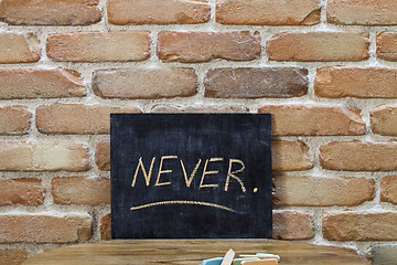 Image showing Chalk board with the word NEVER drown by hand and chalks on wood