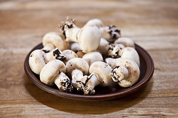 Image showing Fresh raw organic champignons on brown ceramic plate on wooden t