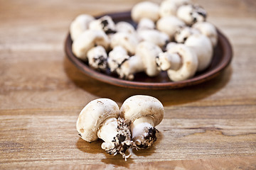 Image showing Fresh raw organic champignons on brown ceramic plate on wooden t