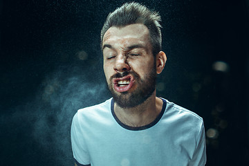 Image showing Young handsome man with beard sneezing, studio portrait