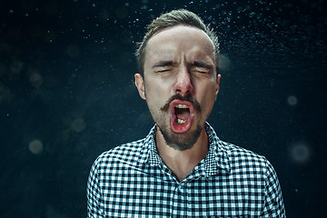 Image showing Young handsome man with beard sneezing, studio portrait