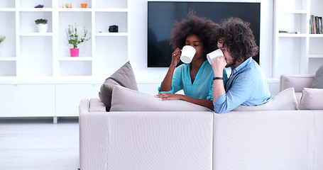 Image showing multiethnic couple sitting on sofa at home drinking coffe