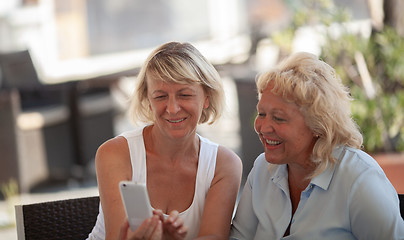 Image showing Two middle aged women sitting outside and smiling while looking at a smartphone screen