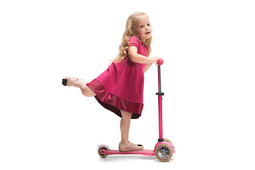 Image showing Smiling cute toddler girl three years riding a scooter over white background