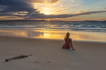 Image showing Female sitting on the sand watching the sunrise