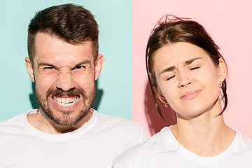 Image showing Closeup portrait of young couple, man, woman. One being excited happy smiling, other serious, concerned, unhappy on pink and blue background. Emotion contrasts