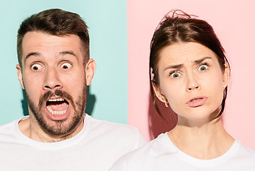 Image showing Closeup portrait of young couple, man, woman. One being excited happy smiling, other serious, concerned, unhappy on pink and blue background. Emotion contrasts