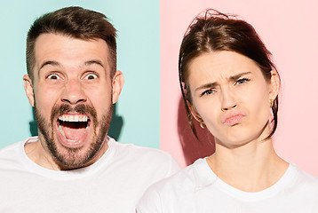 Image showing Closeup portrait of young couple, man, woman. One being excited happy smiling, other serious, concerned, unhappy on pink and blue background. Emotion contrasts