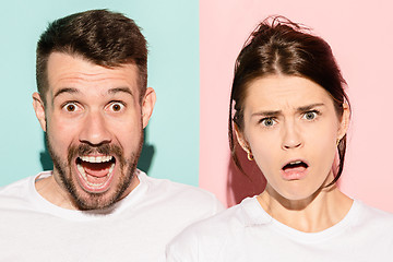 Image showing Closeup portrait of young couple, man, woman. One being excited happy smiling, other serious, concerned, unhappy on pink and blue background. Emotion contrasts