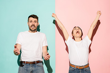 Image showing Closeup portrait of young couple, man, woman. One being excited happy smiling, other serious, concerned, unhappy on pink and blue background. Emotion contrasts