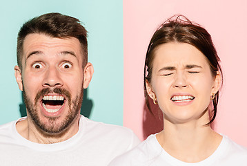 Image showing Closeup portrait of young couple, man, woman. One being excited happy smiling, other serious, concerned, unhappy on pink and blue background. Emotion contrasts