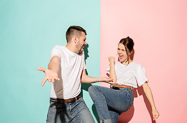 Image showing Closeup portrait of young couple, man, woman. One being excited happy smiling, other serious, concerned, unhappy on pink and blue background. Emotion contrasts