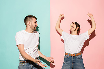 Image showing Closeup portrait of young couple, man, woman. One being excited happy smiling, other serious, concerned, unhappy on pink and blue background. Emotion contrasts