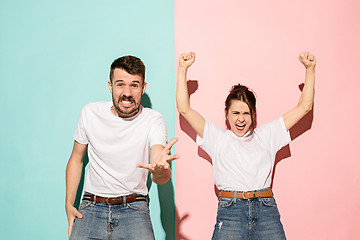 Image showing Closeup portrait of young couple, man, woman. One being excited happy smiling, other serious, concerned, unhappy on pink and blue background. Emotion contrasts