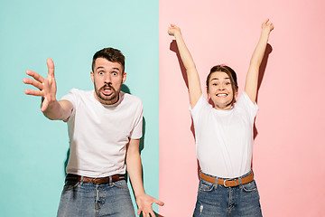 Image showing Closeup portrait of young couple, man, woman. One being excited happy smiling, other serious, concerned, unhappy on pink and blue background. Emotion contrasts