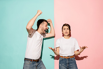 Image showing Closeup portrait of young couple, man, woman. One being excited happy smiling, other serious, concerned, unhappy on pink and blue background. Emotion contrasts