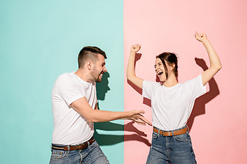 Image showing Closeup portrait of young couple, man, woman. One being excited happy smiling, other serious, concerned, unhappy on pink and blue background. Emotion contrasts