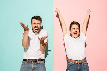 Image showing Closeup portrait of young couple, man, woman. One being excited happy smiling, other serious, concerned, unhappy on pink and blue background. Emotion contrasts