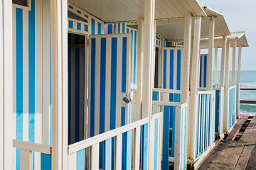 Image showing Striped white and blue striped beach houses and black sandy beach.