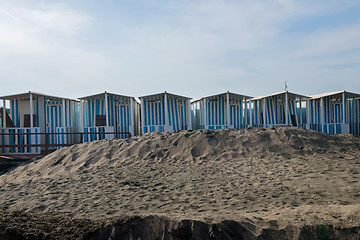 Image showing Striped white and blue striped beach houses and black sandy beach.