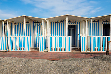 Image showing Striped white and blue striped beach houses and black sandy beach.
