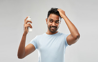 Image showing smiling indian man applying hair spray over gray