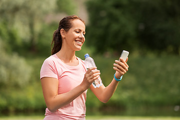 Image showing woman with smartphone drinking water in park