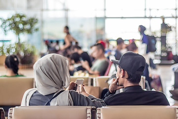 Image showing Modern muslim islamic asian couple using their smartphone apps while sitting and waiting for flight departure at international airport terminal