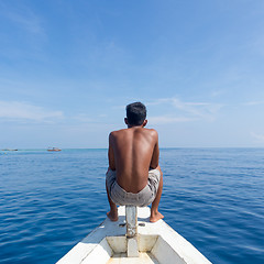 Image showing Local Sporty Guy Sitting Topless at the Bow of Traditional White Wooden Sail Boat, Looking At Beautiful Blue Sea of Gili Islands near Bali, Indonesia