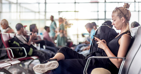 Image showing Female traveler using her cell phone while waiting to board a plane at departure gates at asian airport terminal.