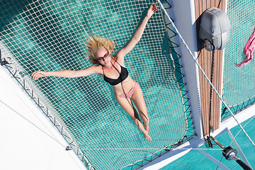 Image showing Woman relaxing on a summer sailing cruise,lying in hammock of luxury catamaran near picture perfect white sandy beach on Spargi island in Maddalena Archipelago, Sardinia, Italy.