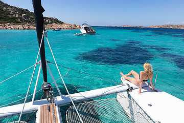 Image showing Woman relaxing on a summer sailing cruise, sitting on a luxury catamaran near picture perfect white sandy beach on Spargi island in Maddalena Archipelago, Sardinia, Italy.