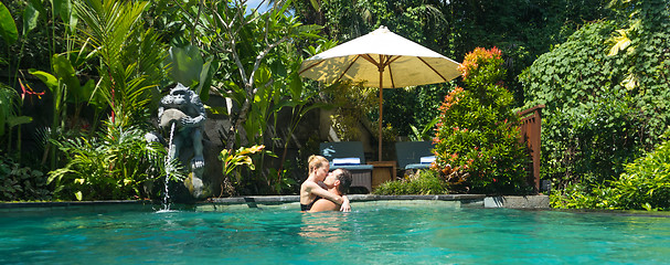 Image showing Happy couple kissing while relaxing in outdoor spa infinity swimming pool surrounded with lush tropical greenery of Ubud, Bali. Luxury spa and wellness vacation retreat concept